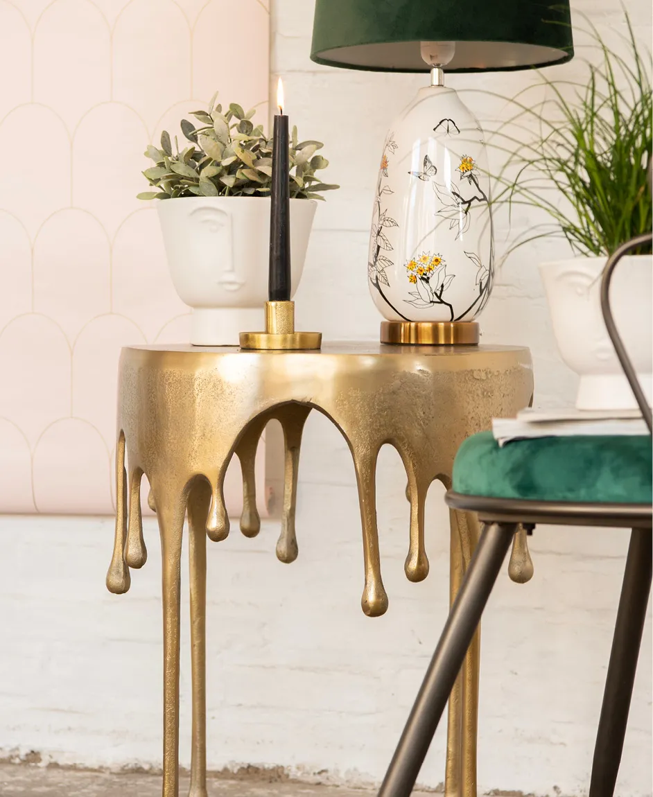 Une table d'appoint, un bougeoir avec une bougie allumée, des pots de fleurs, une lampe de table et une chaise.